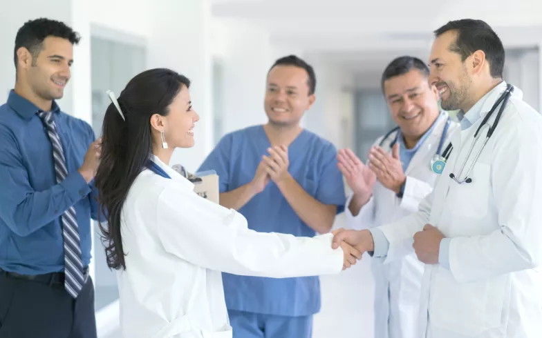 Eine Ärztin gratuliert einem Arzt, das Krankenhauspersonal klatscht im Hintergrund