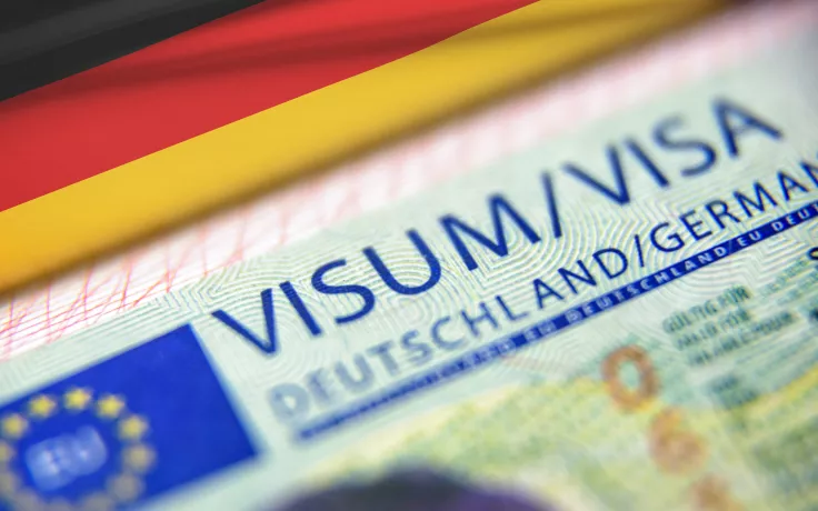 Einleitungsbild: Visum in Deutschland beantragen - ein deutsches Visum in Nahaufnahme neben eine deutschen Fahne