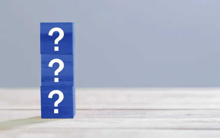 FAQ: Drei Würfel mit Fragezeichen sind auf einem Tisch übereinandergestapelt